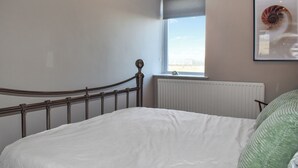 Une chambre à coucher avec un lit, une fenêtre, un radiateur et un tableau encadré au mur.