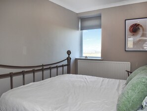 A bedroom with a bed, a window, a radiator, and a framed picture on the wall. - Marina Views, your peaceful coastal escape in the heart of Amble. (Morpeth)
