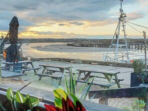 A beachside view with a statue, picnic tables, and a pier. - Marina Views, your peaceful coastal escape in the heart of Amble. (Morpeth)