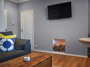 Un salón con pared gris, un televisor de pantalla plana sobre la chimenea, un sofá gris con cojines y una mesa de centro de madera.