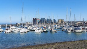 A marina with numerous boats docked, a clear sky, and buildings in the background. - Marina Views, your peaceful coastal escape in the heart of Amble. (Morpeth)