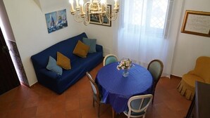 Un comedor con una mesa redonda cubierta con mantel azul, un sofá azul con cojines y una araña.