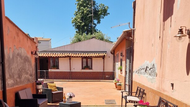 Un patio con suelo de piedra, mobiliario exterior y un edificio con techo de tejas.