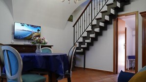 Un comedor con una mesa dispuesta para cuatro, un televisor en la pared y una escalera que conduce a otra habitación.