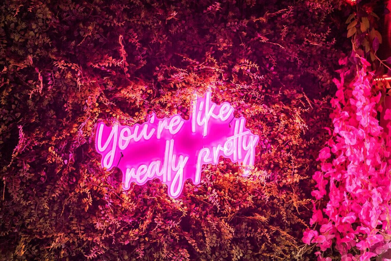 Un letrero de neón con el texto 'You're like really pretty' en medio de una exuberante vegetación.