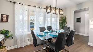 Un espace repas avec une table en verre, des chaises noires, un lustre moderne et une vue dégagée grâce à de grandes fenêtres.