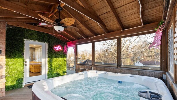 Un bain à remous sous un toit en bois, avec vue sur les arbres et un mur en briques.