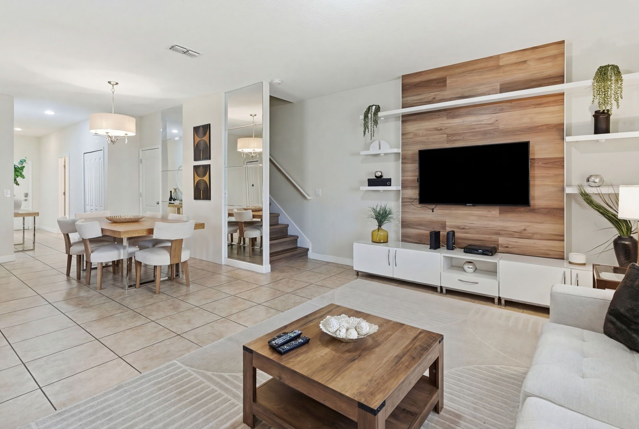 Een moderne woonkamer met een flatscreen-tv, een wand van hout, witte meubels en een eethoek met een ronde tafel en stoelen.