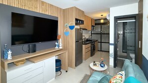 A modern living room with a flat-screen TV, wooden paneling, a kitchen area with a refrigerator, and a small dining table. - Dept. Unique the best of Equipe (Santa Cruz de la Sierra)