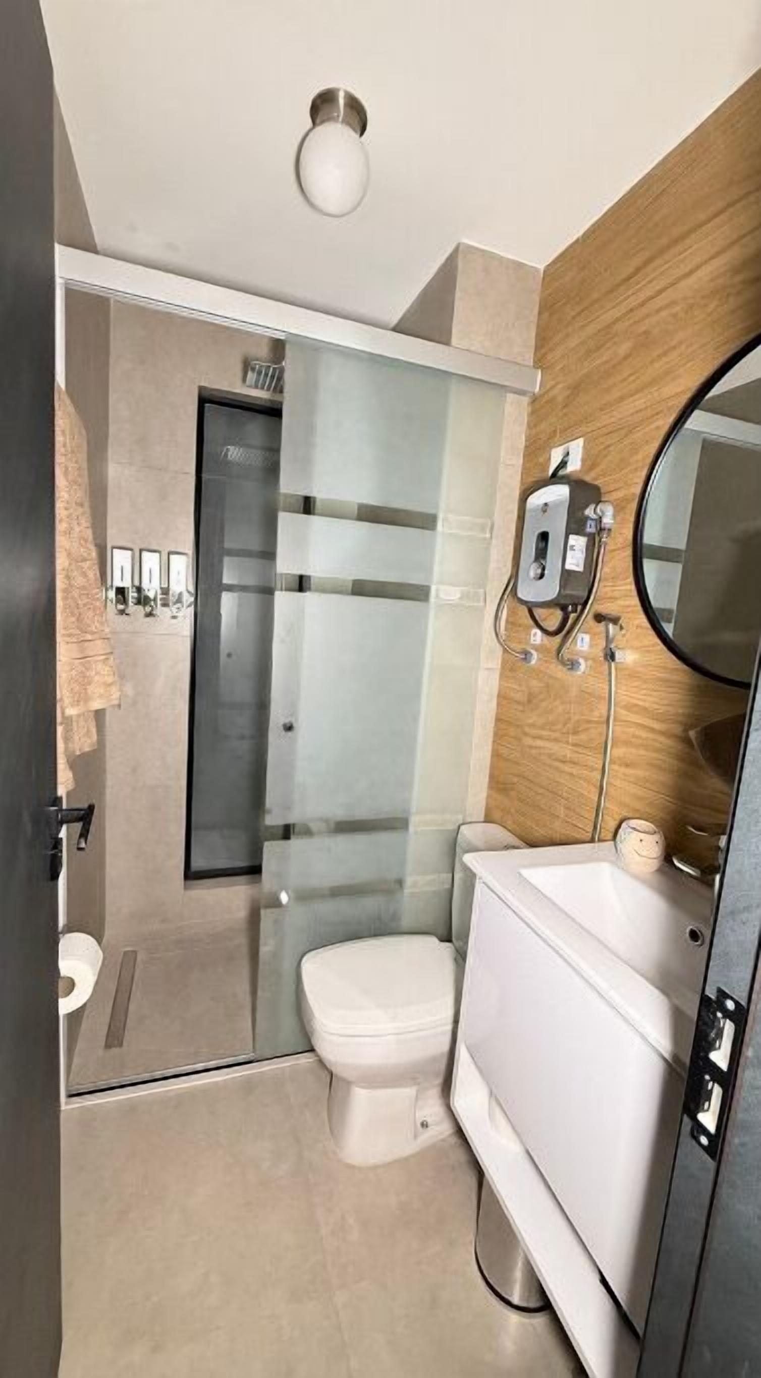 A compact bathroom with a toilet, a glass shower enclosure, and a wooden wall.