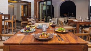 A dining area with wooden tables and chairs, two plates of food, and wine glasses.