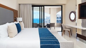 A hotel room with a large bed, a desk, a chair, and a view of the sea.