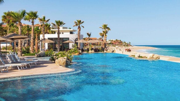 A resort pool with clear blue water, surrounded by palm trees and lounge chairs.