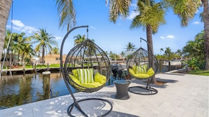 Outdoor seating with wicker chairs and cushions, a water body, and palm trees.