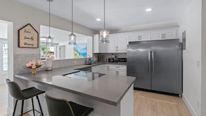 A modern kitchen with a large island, stainless steel appliances, and pendant lighting.