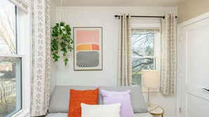 Une chambre à coucher avec un lit, des oreillers, une plante suspendue, une fenêtre et une porte.
