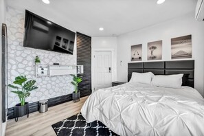 Una camera da letto moderna con un letto grande, una TV montata a parete e tre opere d'arte incorniciate sopra il letto.