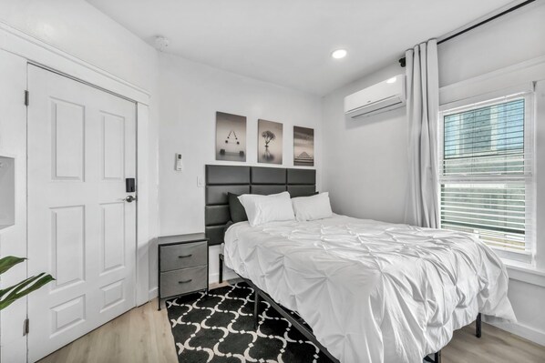 Une chambre à coucher moderne avec un lit blanc, une tête de lit grise et un tapis à motifs noir et blanc.
