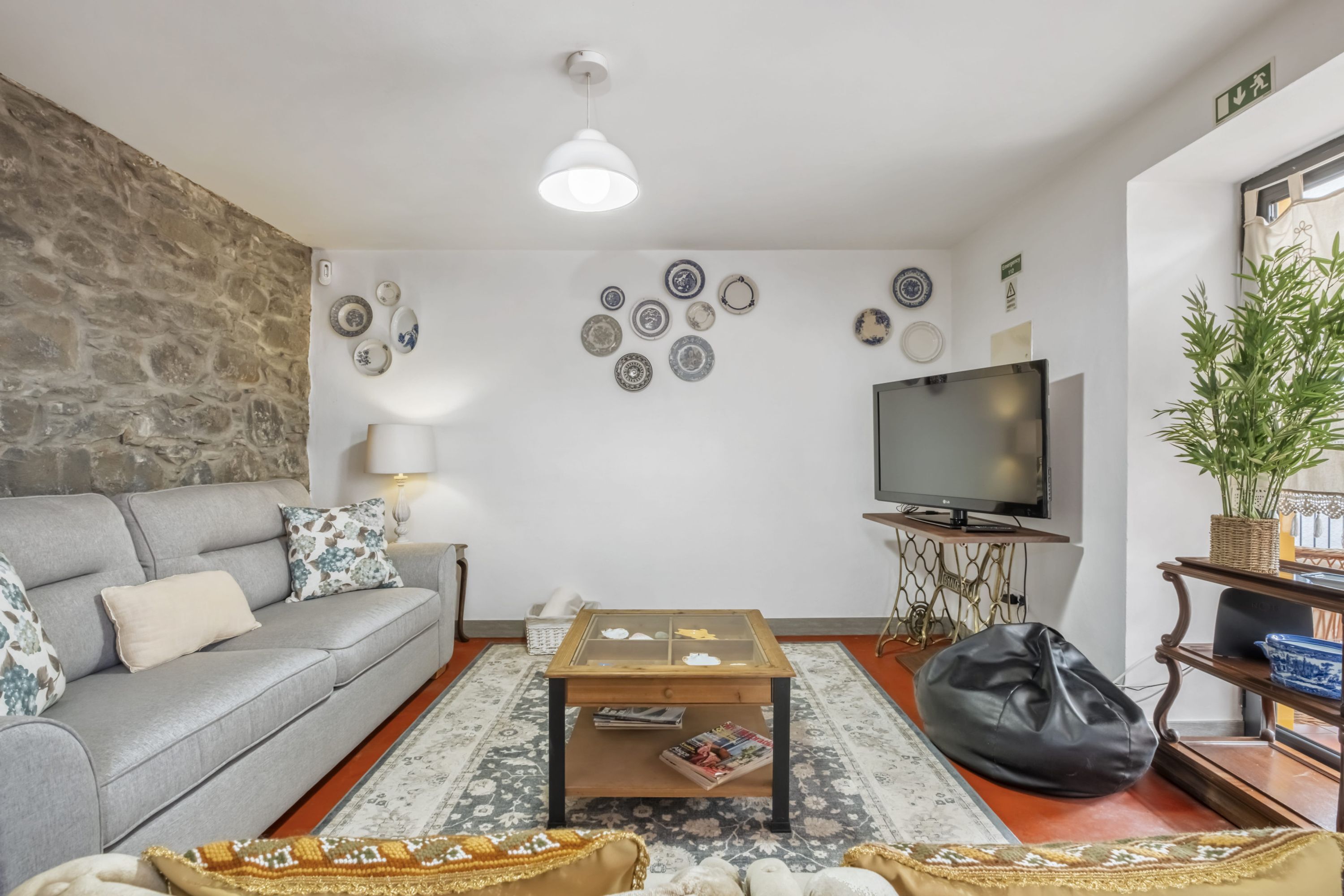 A living room with a grey sofa, a coffee table, a television, and decorative plates on the wall.