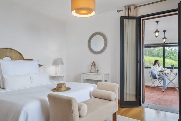 Une chambre à coucher avec un lit, des tables de chevet, une commode, une chaise, une fenêtre et une vue sur une personne assise à l’extérieur.