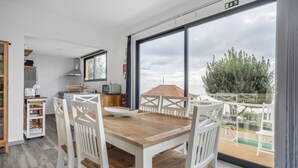 A modern kitchen with white cabinetry, a wooden dining table, and a large window overlooking a balcony. - Villa Piedade by Homie (Ponta do Sol)