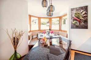 Un espace repas avec une table en verre, des éléments décoratifs en bois et une vue dégagée grâce à de grandes fenêtres.
