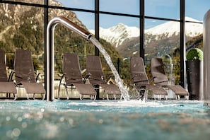 Una piscina interna con vista su montagne innevate attraverso ampie finestre.