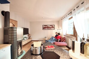 Une cuisine moderne équipée d’un poêle à bois, d’un coin repas avec une table et des chaises, et d’une fenêtre avec des rideaux.