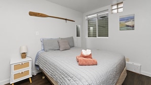 A bedroom with a bed, a wooden paddle, a window, and a painting on the wall.