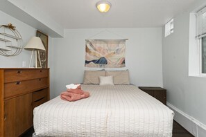 Un dormitorio con una cama, un aparador de madera, un tapiz colgante y una ventana con persianas.