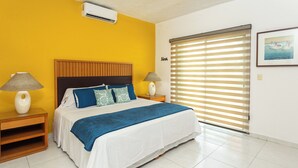 Ein Schlafzimmer mit einem Bett, zwei Nachttischen, einem Fenster mit Jalousien und einer Wand-Klimaanlage.