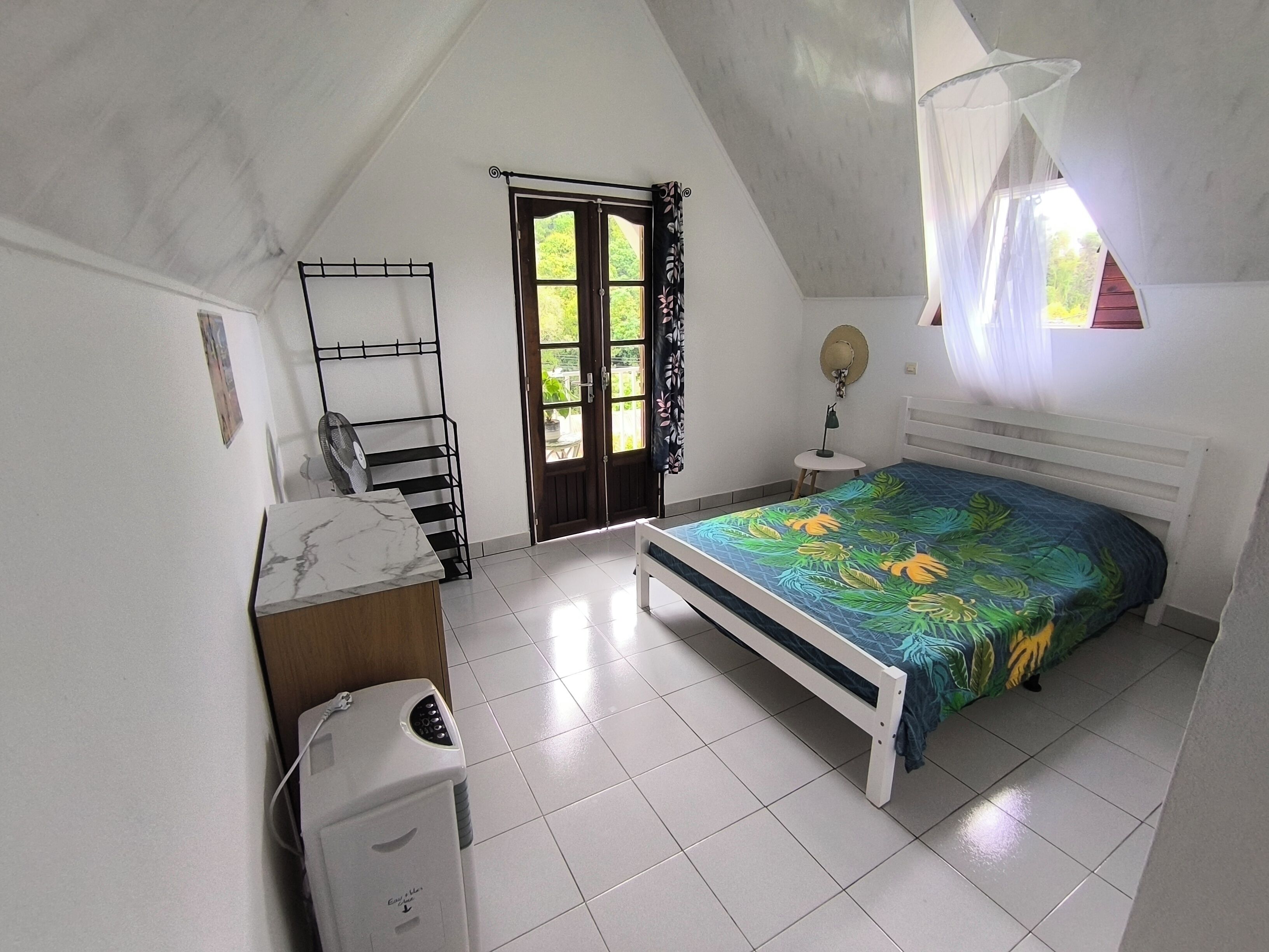 A bedroom with a bed, a bedside table, a fan, a heater, and a window with curtains.