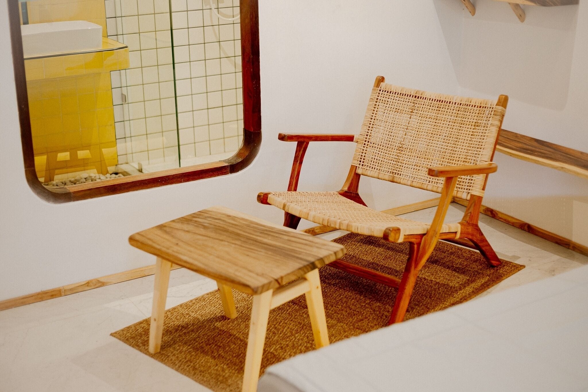 Una habitación pequeña con una silla de madera, una mesita y una ventana con diseño de cuadrícula.