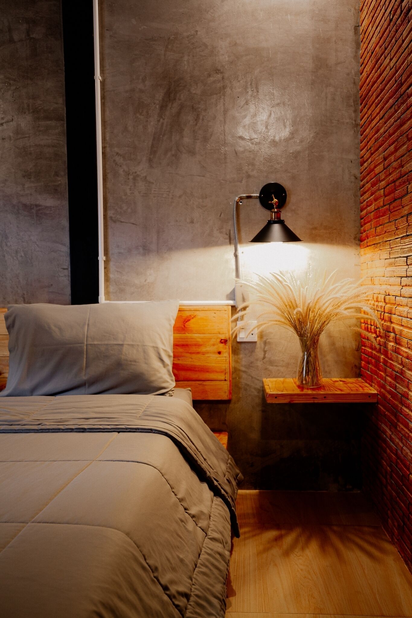 A bedroom with a bed, bedside table, lamp, and a vase with dried plants.