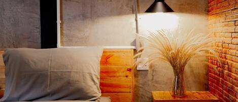 A bedroom with a bed, bedside table, lamp, and a vase with dried plants.