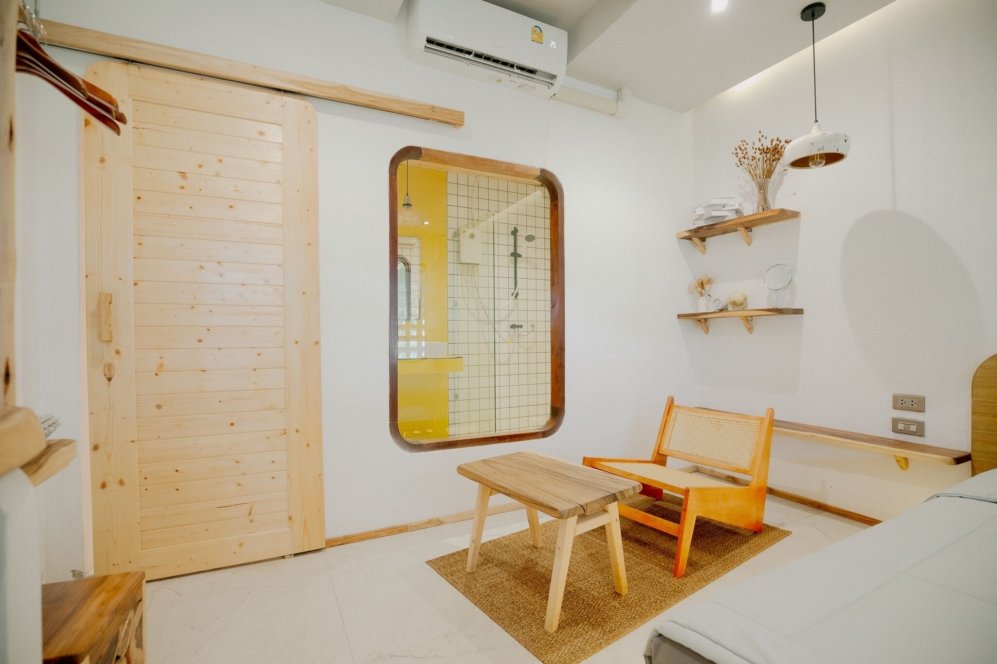 Une pièce avec une porte en bois, une petite table en bois, un banc, un miroir et une étagère ornée d’objets décoratifs.
