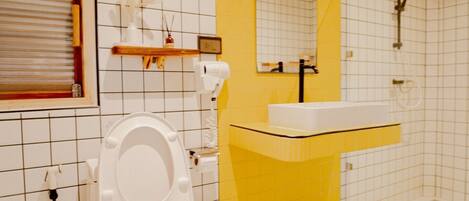 Et badeværelse med et hvidt toilet, en gulvbelagt vask og en bruser.