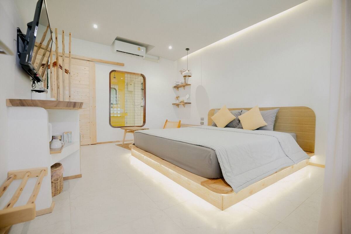 A modern bedroom with a bed, wooden headboard, shelves, and a TV mounted on the wall.