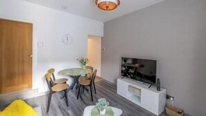A modern living room with a round dining table, chairs, a flat-screen TV, and a white entertainment unit.