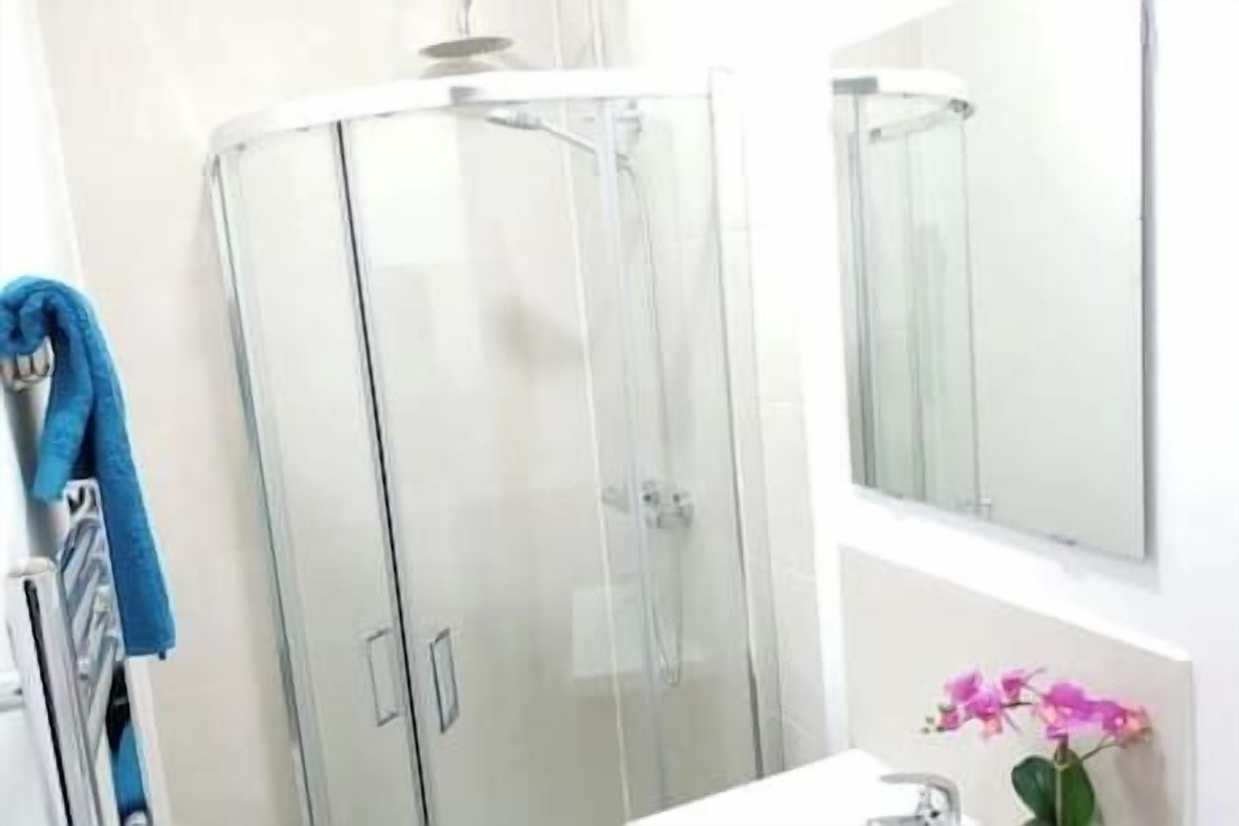 A bathroom with a glass-enclosed shower, a white sink, and a mirror.