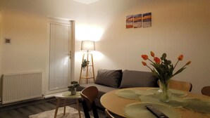 A cozy living room with a sofa, a dining table with placemats, a lamp, and a vase with flowers.