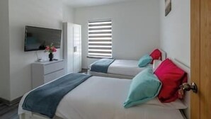 A bedroom with two beds, a TV, a window with blinds, and a wooden door.