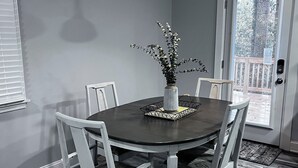 Ein Essbereich mit einem runden Tisch, weißen Stühlen, einer Blumenvase und einer Pendelleuchte.