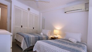 A bedroom with two beds, a ceiling fan, an air conditioning unit, and a bedside lamp.