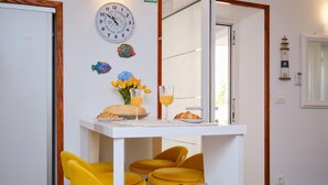 Quarto com relógio de parede branco, uma mesa pequena com itens de café da manhã e duas cadeiras amarelas.