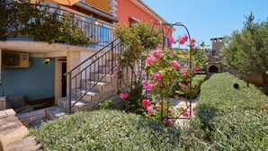 Um edifício com escadaria que leva a uma varanda, rodeado por vegetação exuberante e flores cor-de-rosa.