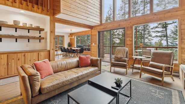 Un vaste espace de vie comprenant un canapé en cuir, une table basse et des meubles en bois. De grandes fenêtres offrent une vue sur les arbres et une terrasse.