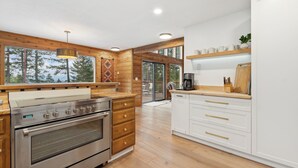 Une cuisine moderne dotée de meubles en bois, d’appareils électroménagers en acier inoxydable et de grandes fenêtres offrant une vue sur l’extérieur.