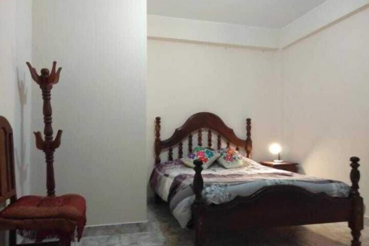 Un dormitorio con una cama de madera, una silla y una mesita de noche con una lámpara.
