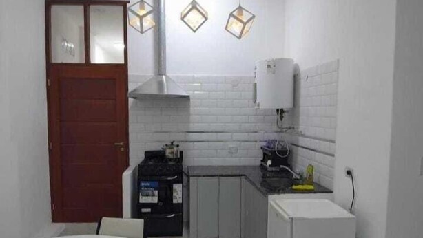 Una cocina compacta con salpicadero blanco de azulejos, una estufa, un fregadero y un refrigerador. Hay luces colgantes sobre la encimera.